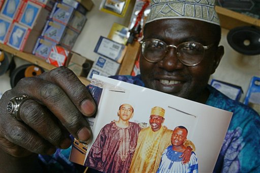 FILE - This Tuesday, Sept. 14, 2004 file photo shows Malik Obama, the older brother of  US President Barack Obama, who holds an undated picture of Barak, left, and himself, center, and an unidentified friend in his shop in Siaya, eastern Kenya. President Barack Obama's polygamist half brother in Kenya has married a woman who is more than 30 years younger than him. The 19-year-old's mother told The Associated Press on Friday Oct. 15, 2010 she is furious that her daughter quit high school and married the 52-year-old. Malik Obama, who is Muslim, has two other wives. Polygamy is legal in Kenya if it falls under religious or cultural traditions.  (AP Photo/Karel Prinsloo)