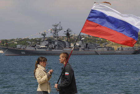 A man holding a Russian flag speaks with a girl wearing a telnyashka, a traditional navy sailor's striped vest, under her jacket during a naval parade to mark the 225th anniversary of Russian navy's Black Sea fleet at the Crimean Peninsula port of Sevastopol, Ukraine, Sunday, May 11, 2008, with the Russian Smetlivy destroyer in the background.(AP Photo/Sergei Chuzavkov)